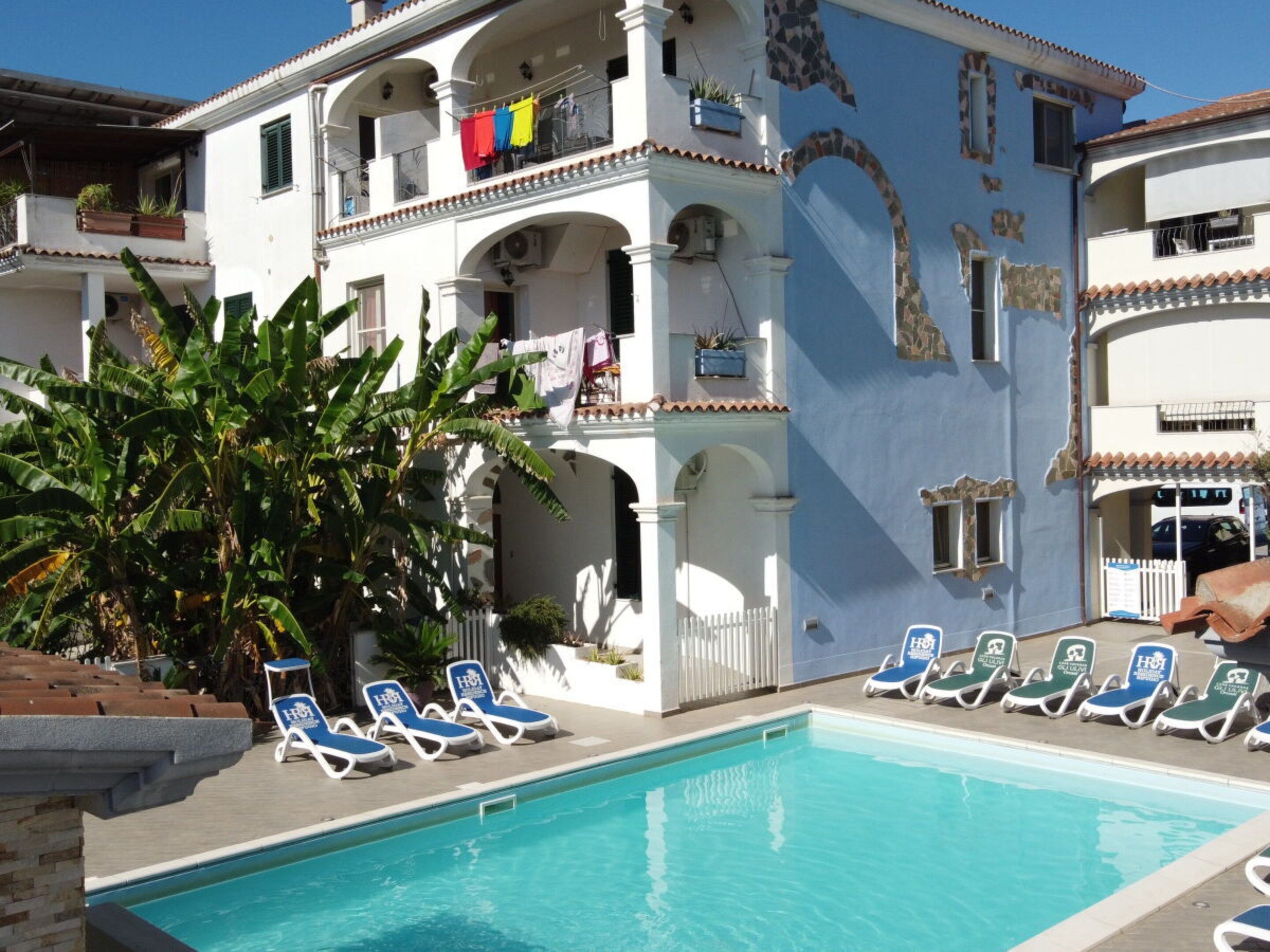 Zona de piscina con sillones de descanso y un edificio con balcones.