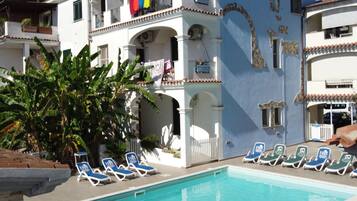 Zona de piscina con sillones de descanso y un edificio con balcones.