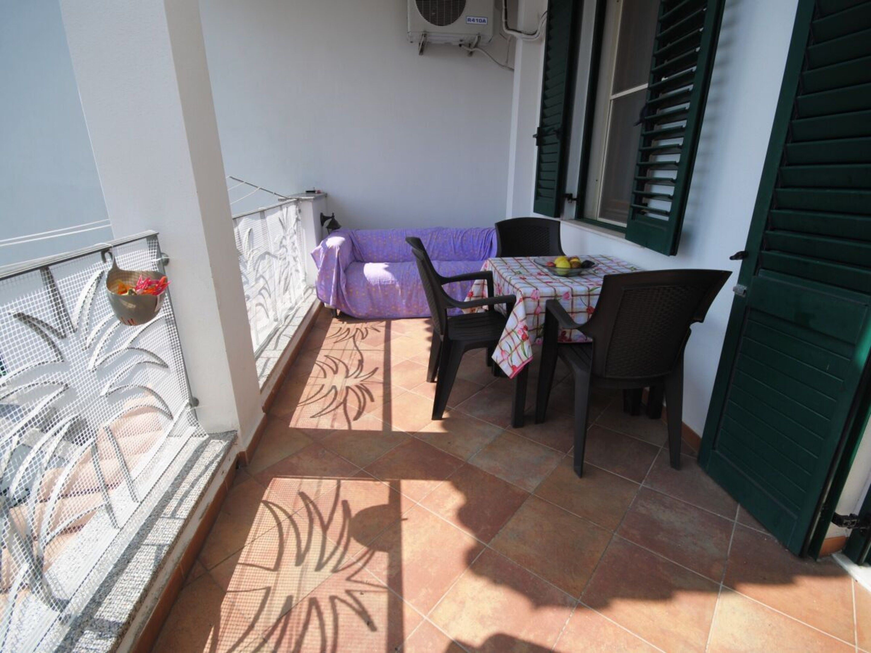 Un pequeño balcón al aire libre con una mesa, sillas, un sofá y un cuenco decorativo.