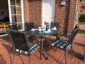 Eine Terrasse im Freien mit einer Ziegelwand, einem Tisch für vier Personen und vier Stühlen mit Kissen.