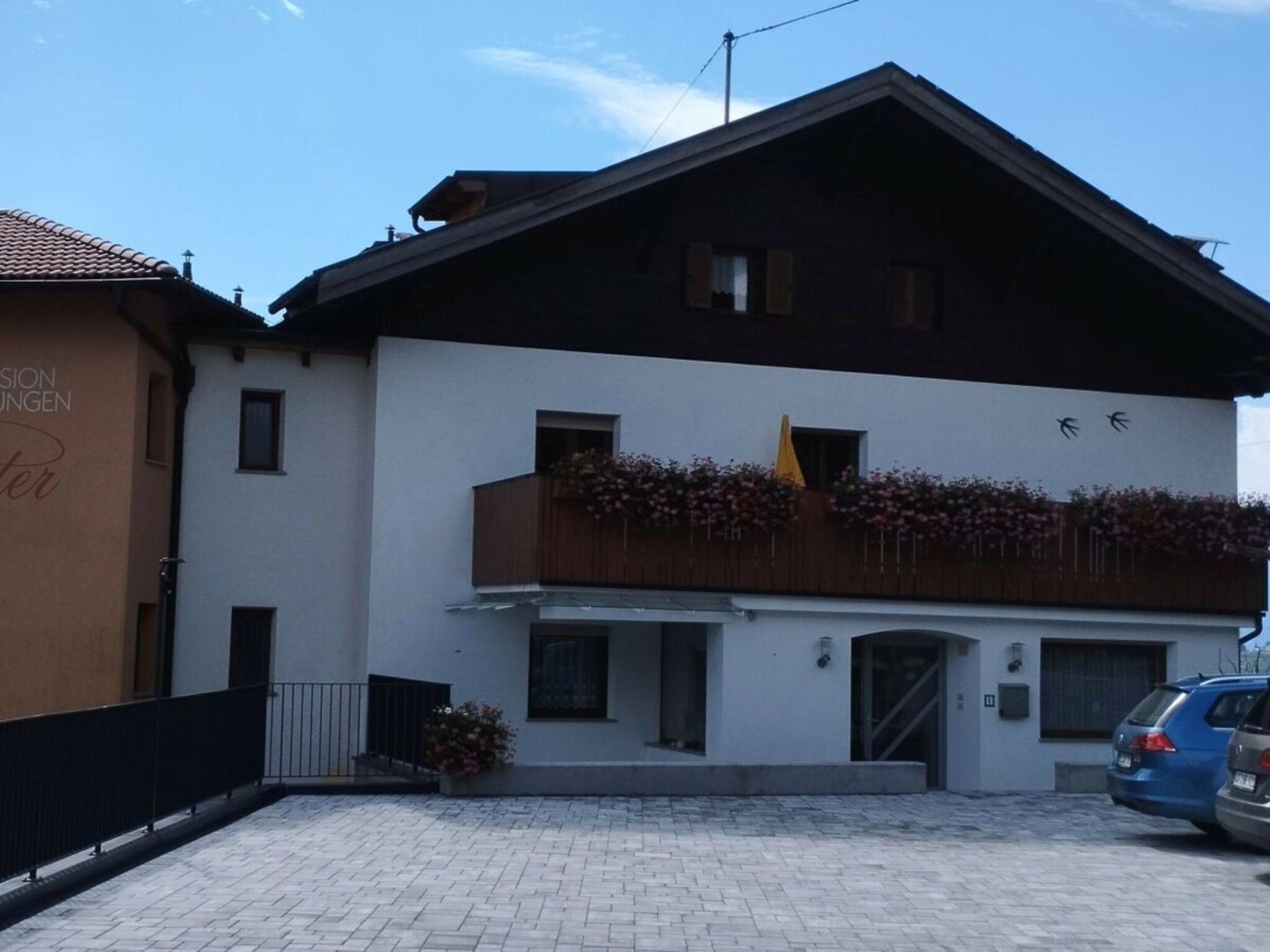 Un edificio su due piani con un balcone, un'auto parcheggiata davanti e un cielo sereno.