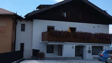 Un edificio su due piani con un balcone, un'auto parcheggiata davanti e un cielo sereno.