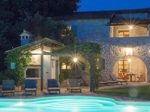 Ein Gebäude aus Stein mit einem Pool, Sitzgelegenheiten im Freien und einer Pergola mit Beleuchtung.