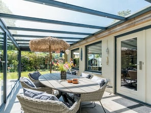 A covered outdoor dining area with a round table, wicker chairs, and a thatched umbrella. - Holiday Home in Renesse With Swimming Pool (Renesse)