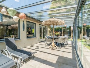 A sunlit patio with a glass enclosure, wicker furniture, and a table with chairs. - Holiday Home in Renesse With Swimming Pool (Renesse)