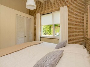 A bedroom with a brick wall, a window with curtains, a bed with patterned pillows, and a white wardrobe. - Holiday Home in Renesse With Swimming Pool (Renesse)