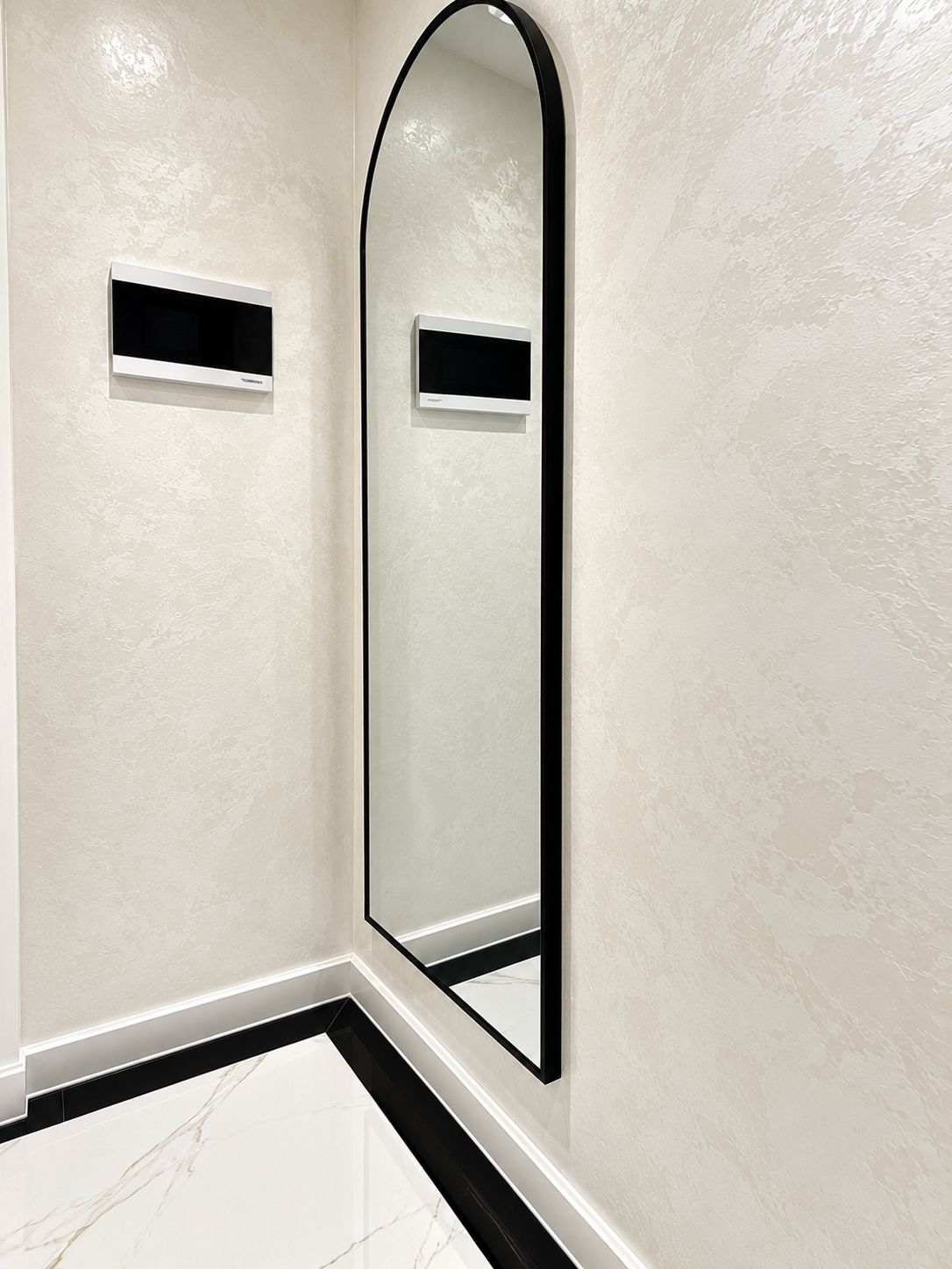 Un baño con un espejo grande, paredes blancas con textura y suelo de mármol.