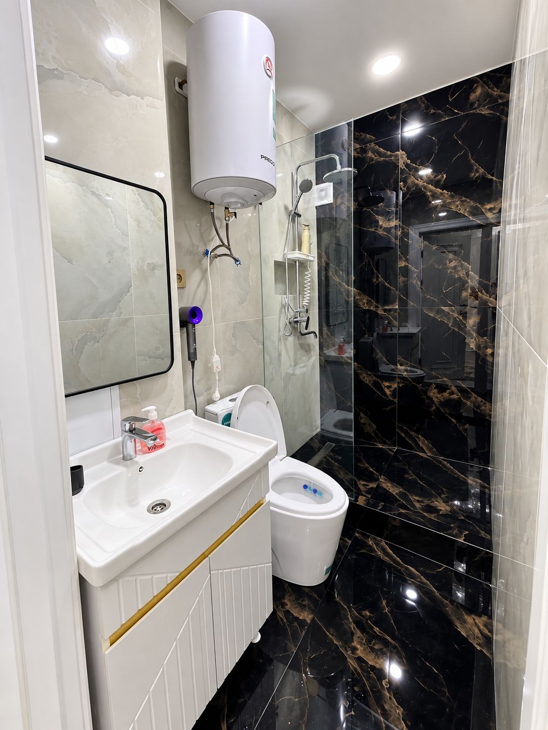 Un baño moderno con lavamanos, inodoro y zona de ducha blancos.