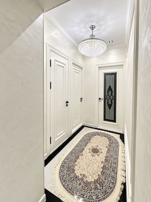 A hallway with a patterned rug, white doors, and a chandelier. - URBAN NEST SAMARKAND LUXE DESIGN APARTMEN (Samarkand)