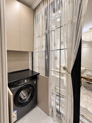 Un área de lavandería compacta con lavadora, un armario y una ventana con cortinas translúcidas.
