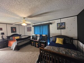 Ein Schlafzimmer mit einem Bett, einem Babybett, einem Deckenventilator und Spielautomaten.