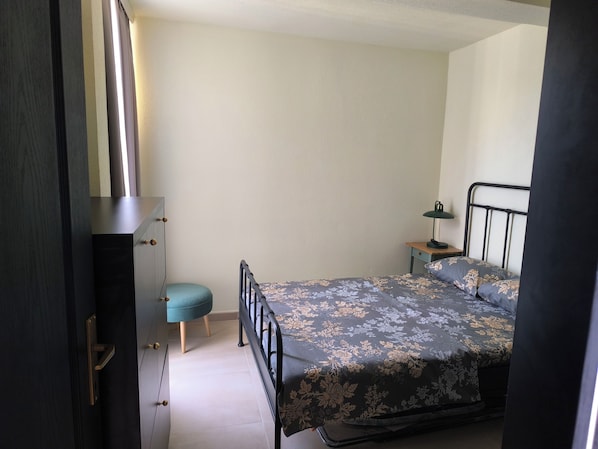 Een slaapkamer met een bed, nachtkastje, lamp en een kledingkast.