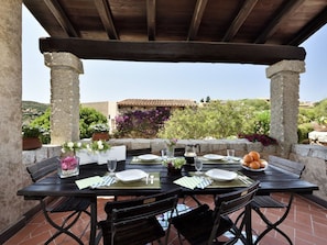 An outdoor dining area with a table set for two, surrounded by stone columns and potted plants. - L"ea di Lavru - Apt 4 (Loiri Porto San Paolo)