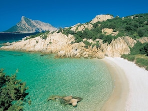A coastal landscape with clear turquoise waters, a sandy beach, and rocky cliffs. - L"ea di Lavru - Apt 4 (Loiri Porto San Paolo)