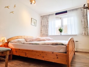 A bedroom with a wooden bed, a bedside table with a lamp, a window with curtains, and a wall-mounted picture. - Do09 Holiday Home Domburg (Domburg)