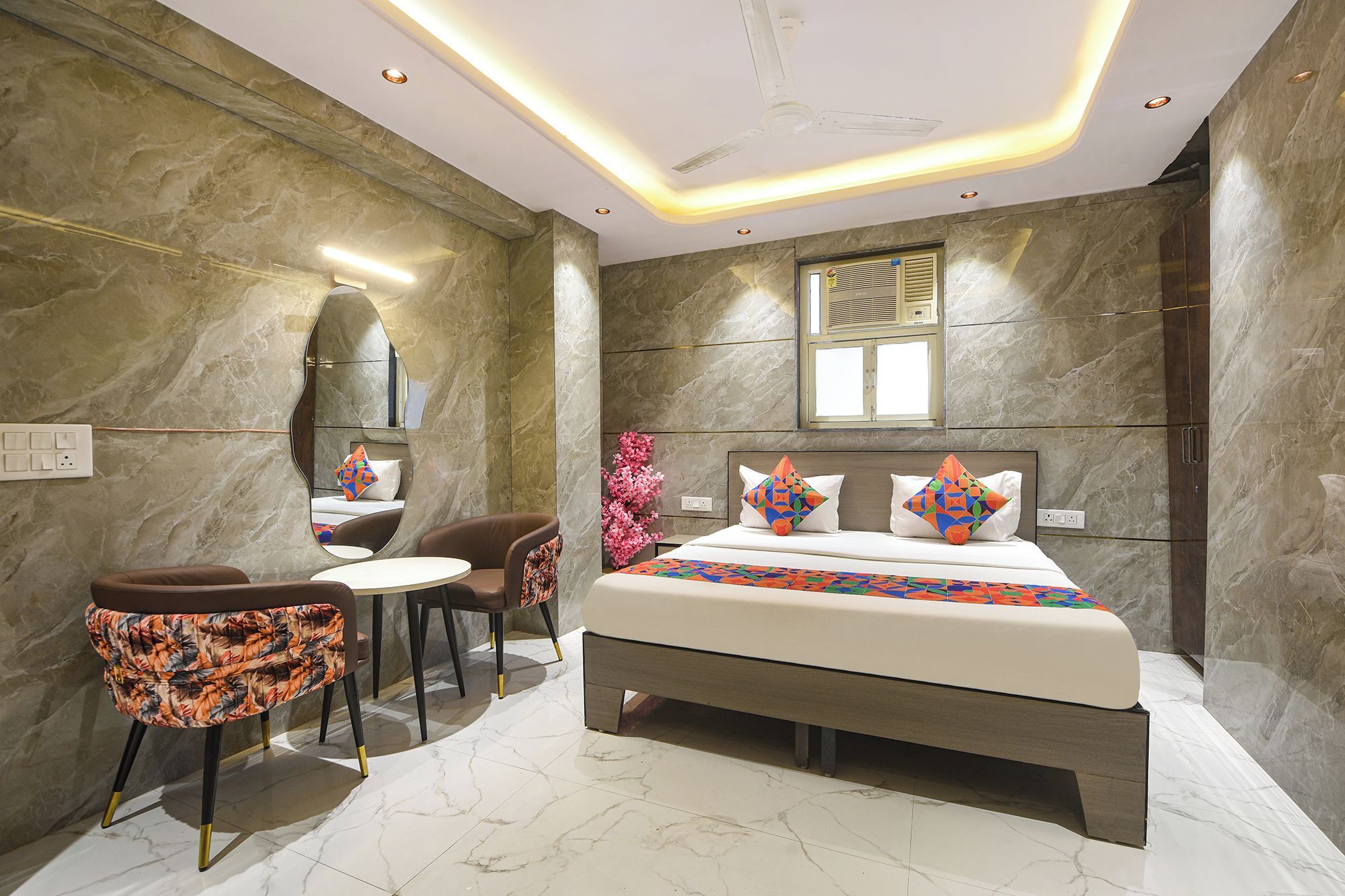 A modern bedroom with a large bed, a small table, two chairs, and a mirror on the wall.