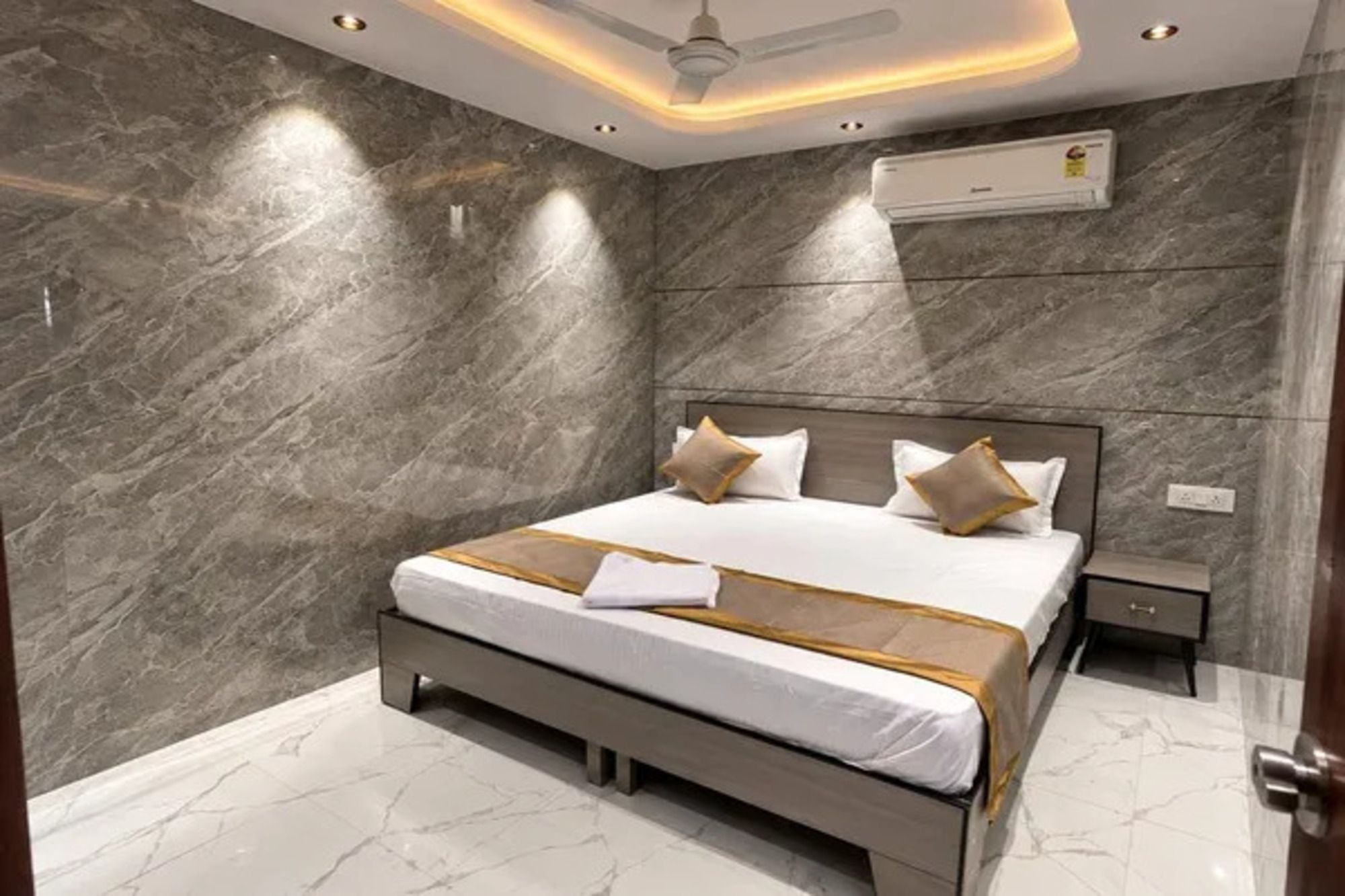 A modern bedroom with a marble wall, a bed with a white and gold bedspread, and a ceiling fan.