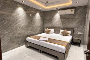 Un dormitorio moderno con pared de mármol, cama con cubrecama blanco y dorado, y ventilador de techo.