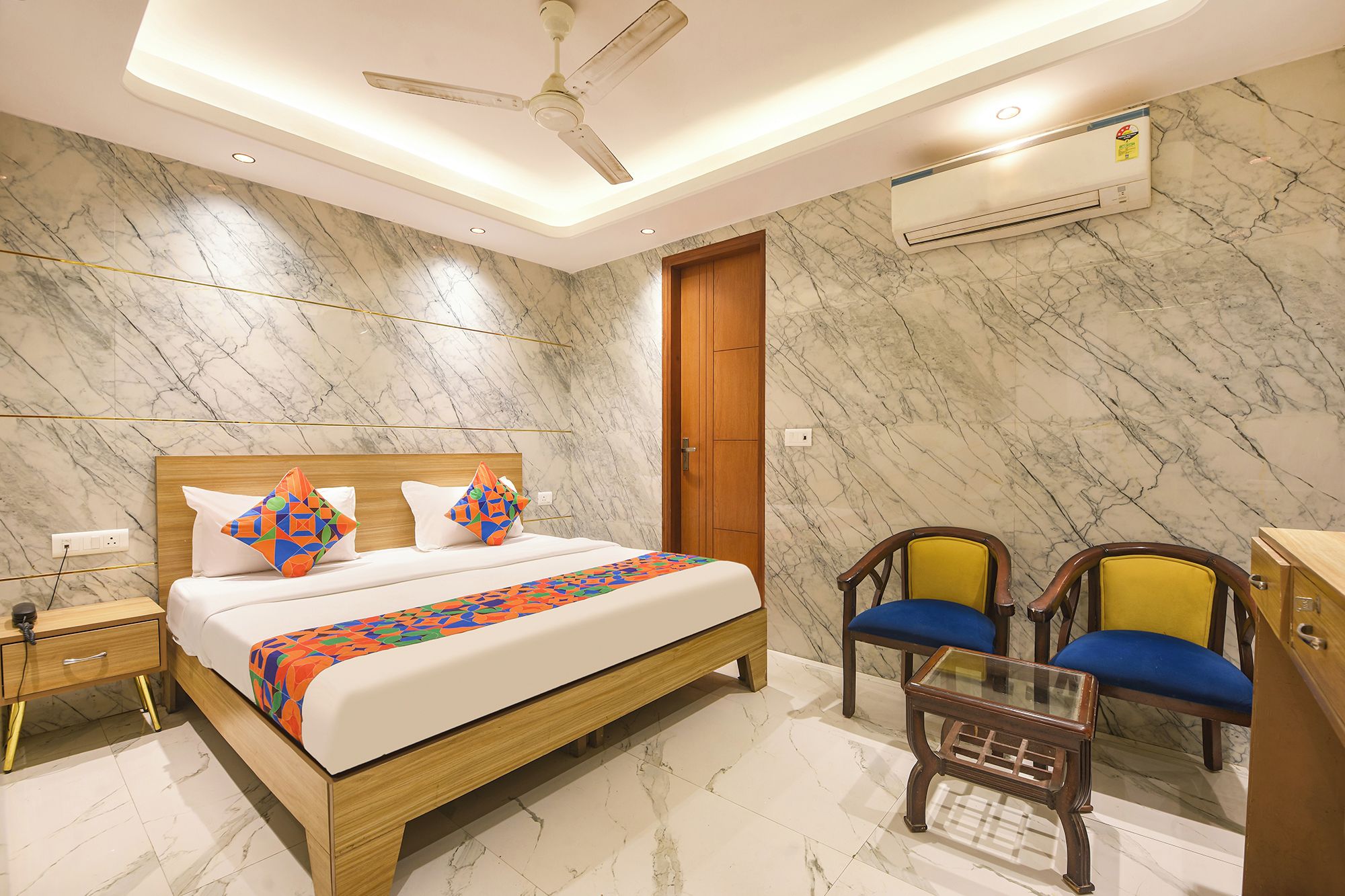 A hotel room with a bed, bedside table, nightstand, chairs, and a small table.