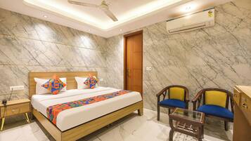 A hotel room with a bed, bedside table, nightstand, chairs, and a small table.