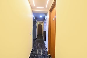 Un pasillo de hotel con piso de mármol, una puerta de madera a la derecha y un letrero de salida en la pared.