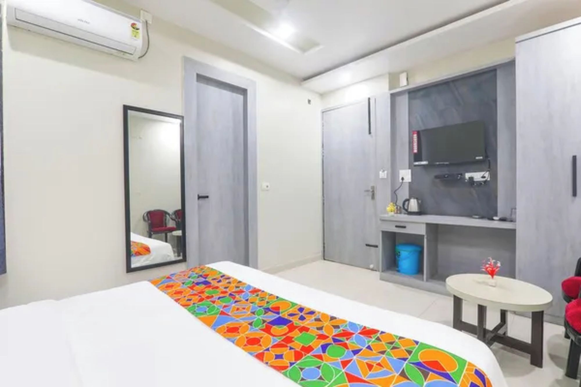 A hotel room with a bed, a mirror, a wardrobe, a television, and a small round table.