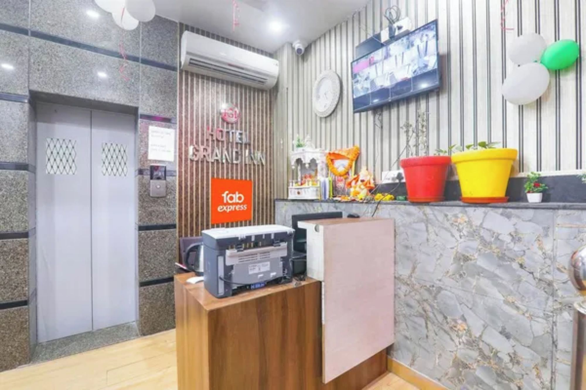 A hotel reception area with a marble wall, a clock, a television, and a 'fab express' sign.
