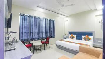 Una habitación de hotel con una cama, un escritorio con una silla, una mesita pequeña y un ventilador de techo.