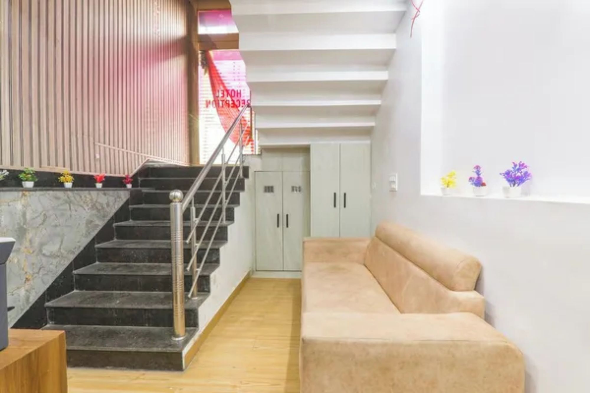 A hotel lobby with a staircase, a beige sofa, and a wall with potted plants.
