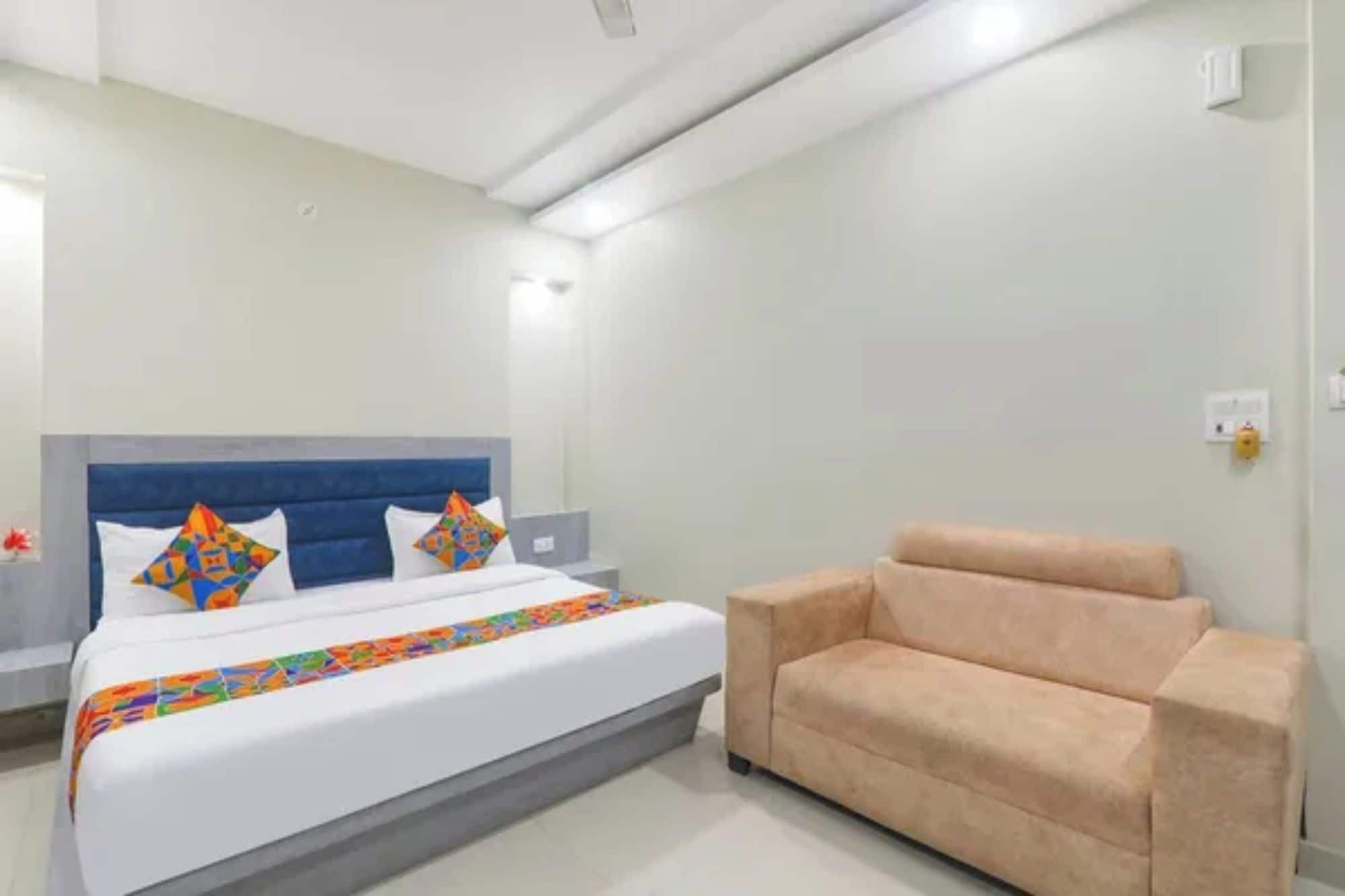 A hotel room with a bed, a sofa, a nightstand, and a wall-mounted light.