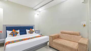 A hotel room with a bed, a sofa, a nightstand, and a wall-mounted light.