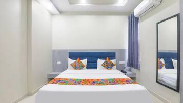 Una habitación de hotel con una cama, una mesita de noche, un equipo de aire acondicionado y un espejo grande en la pared.