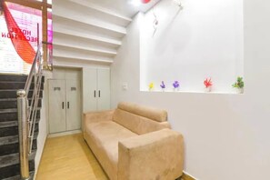 Una habitación con un sofá color beige, una escalera y una ventana con pequeñas plantas.
