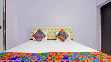 Ein Schlafzimmer mit einem gesteppten Kopfteil, zwei Kissen mit geometrischen Mustern und einer farbenfrohen, geometrisch gemusterten Tagesdecke.