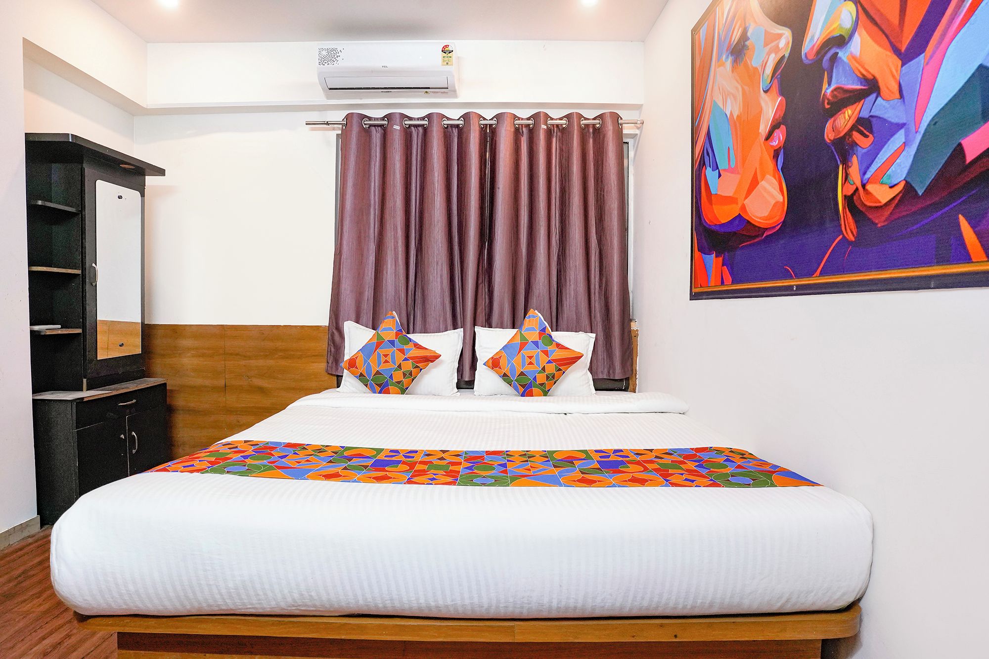 A hotel room with a bed, a dresser, a mirror, a painting, and a window with curtains.