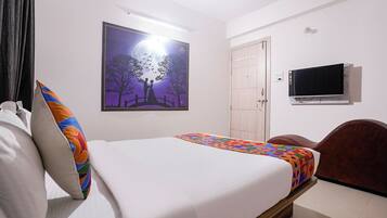 Un dormitorio con cama, televisor, puerta y una pared con un cuadro enmarcado.