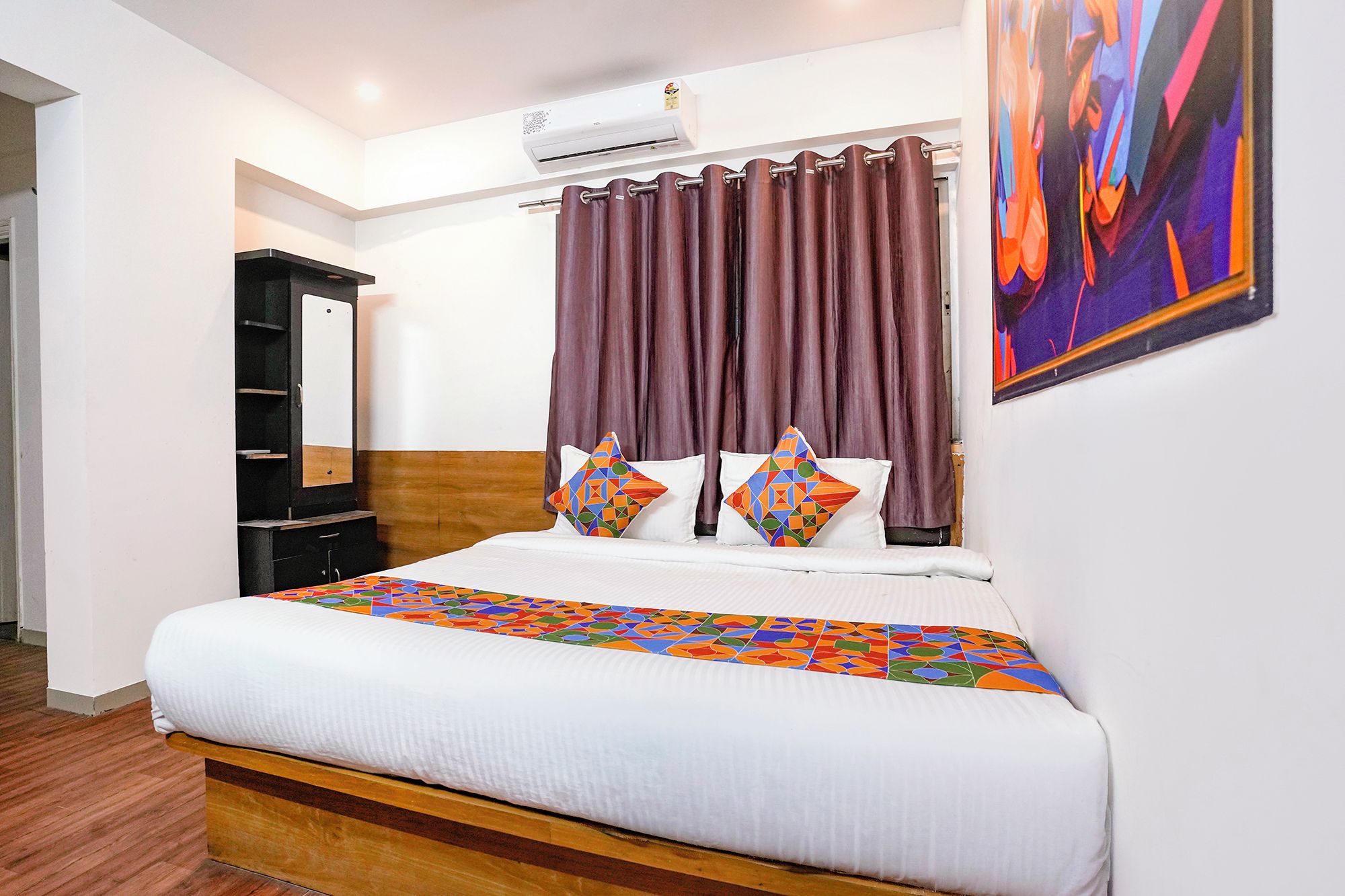 Habitación de hotel con cama, cabecera, aire acondicionado de pared, un cuadro y una ventana con cortinas.