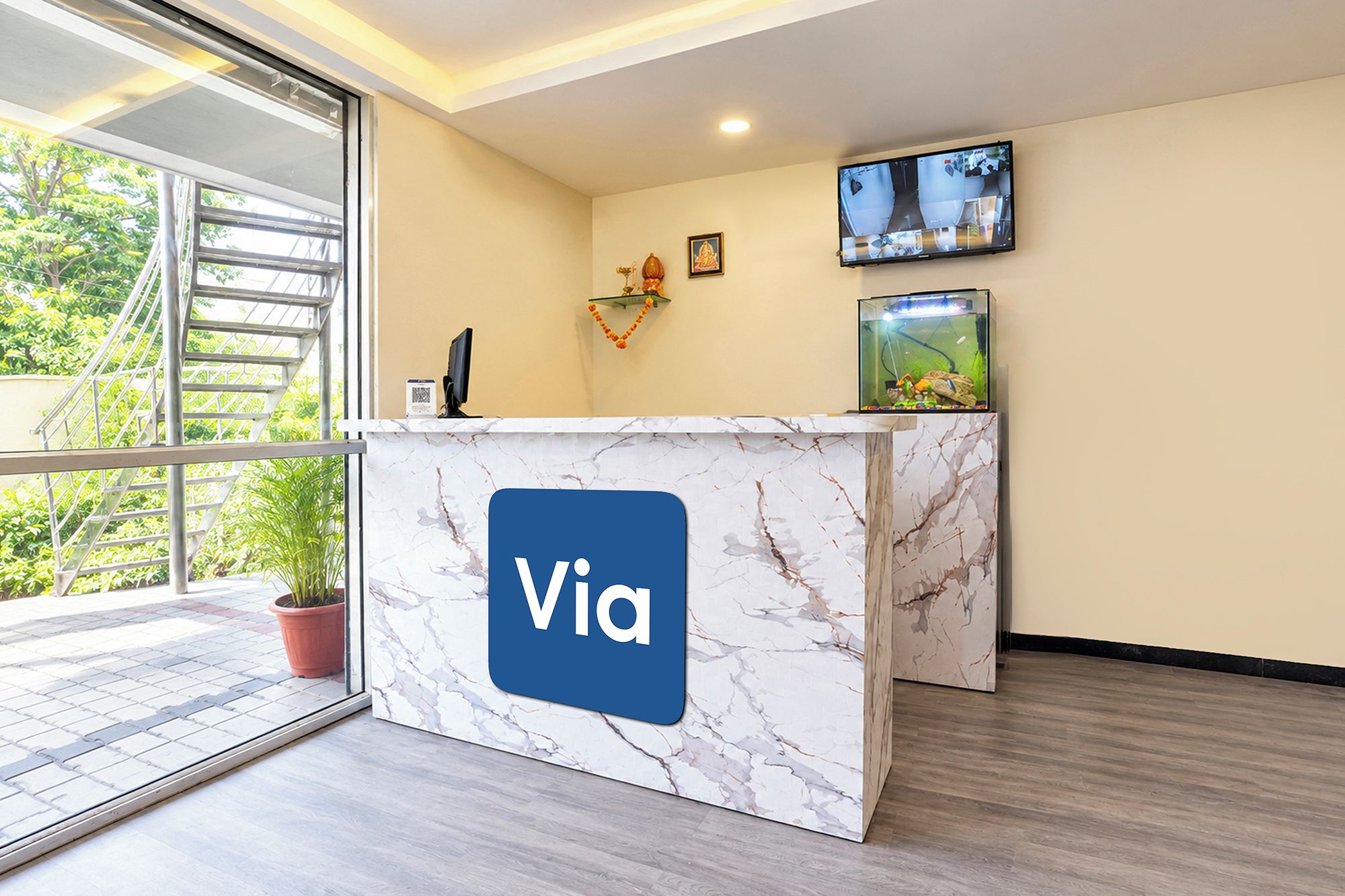 Un mostrador de recepción con diseño de mármol y el logo 'Via', un televisor montado en la pared y una planta en maceta.