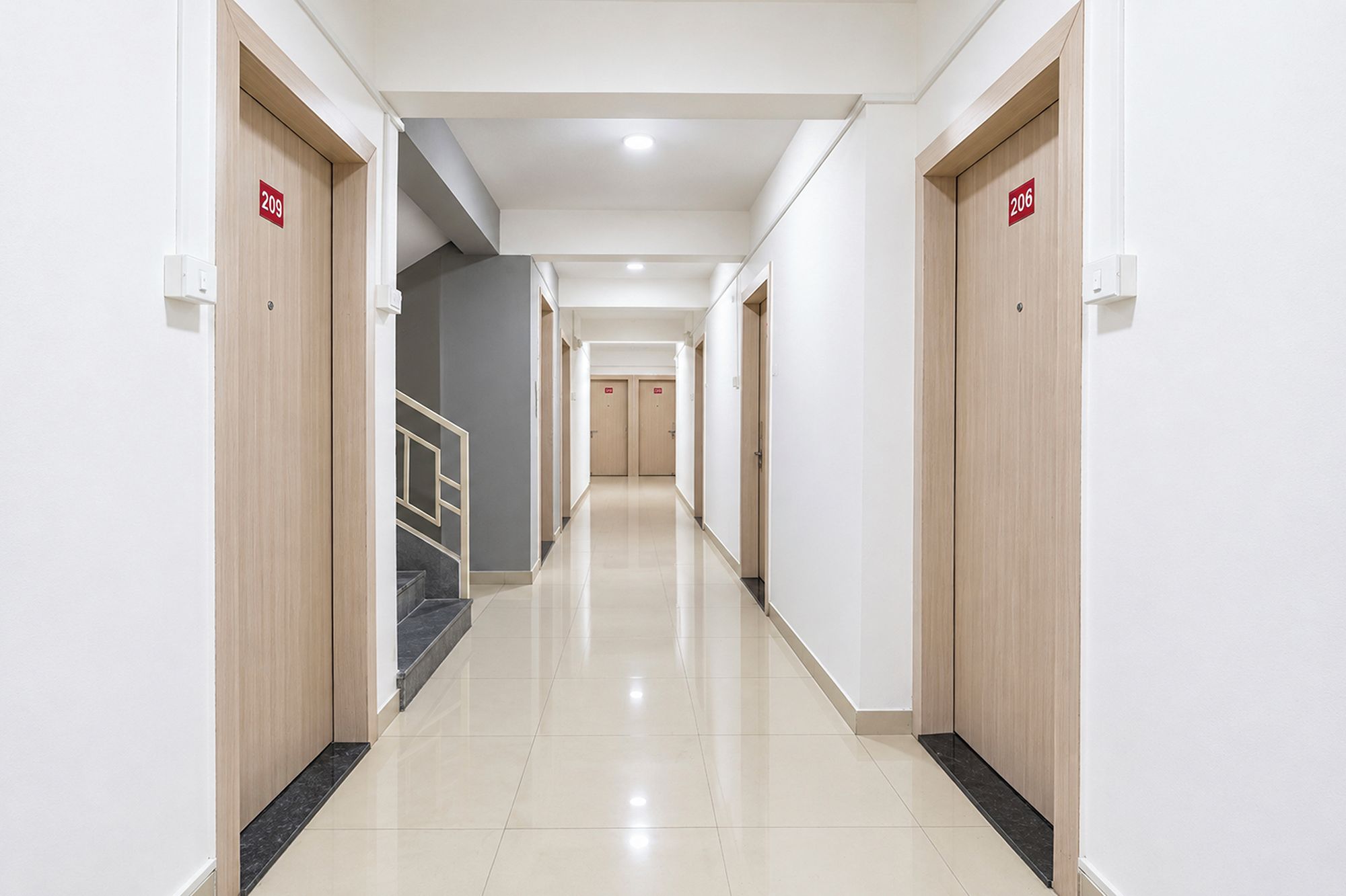 Un pasillo de hotel con puertas numeradas 209 y 206, una escalera y un suelo de baldosas impecable.