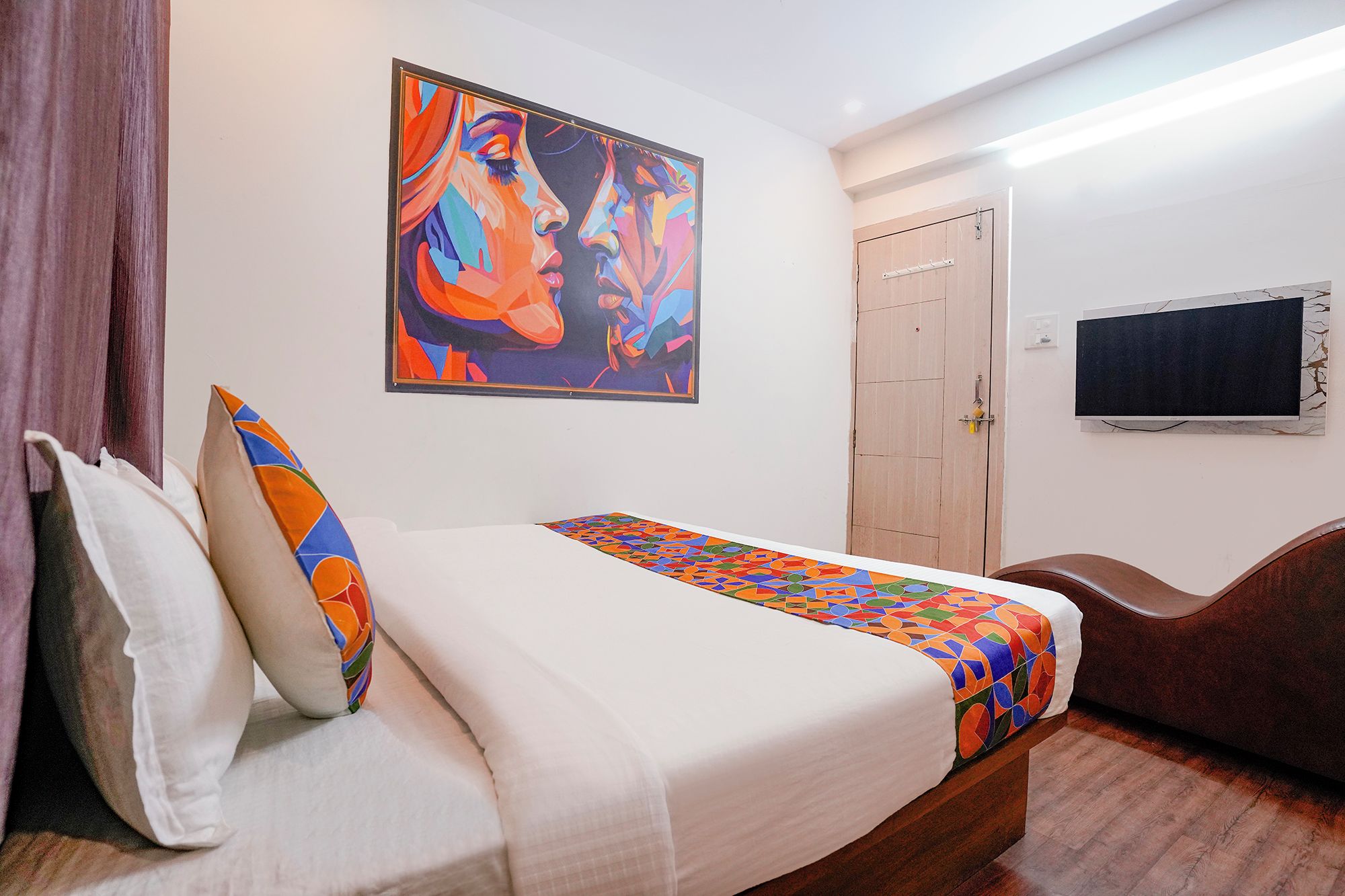 Una habitación de hotel con cama, almohadas, un cuadro, un televisor y una puerta.
