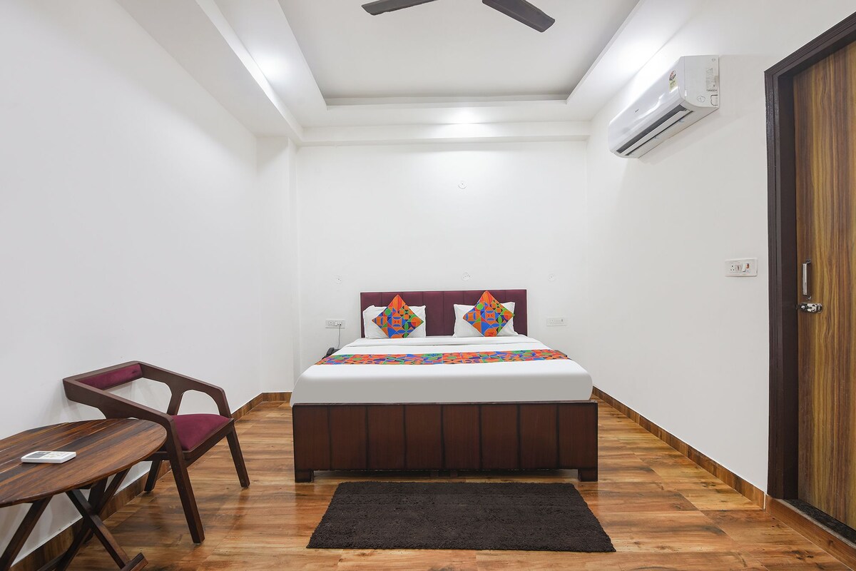 A bedroom with a bed, a chair, a wooden floor, a ceiling fan, and an air conditioning unit.