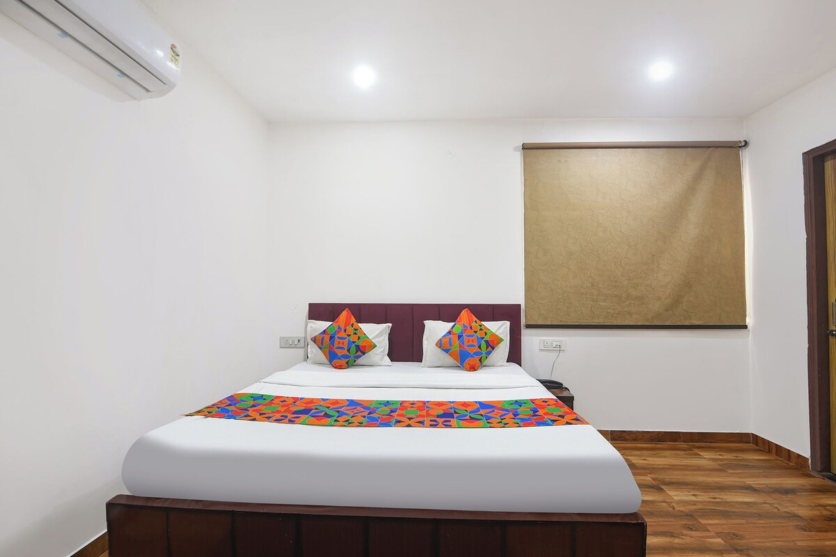 A hotel room with a bed, a window with a blind, and a wooden floor.