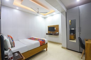Quarto com cama, escrivaninha, guarda-roupa, ventoinha no teto e televisão na parede.