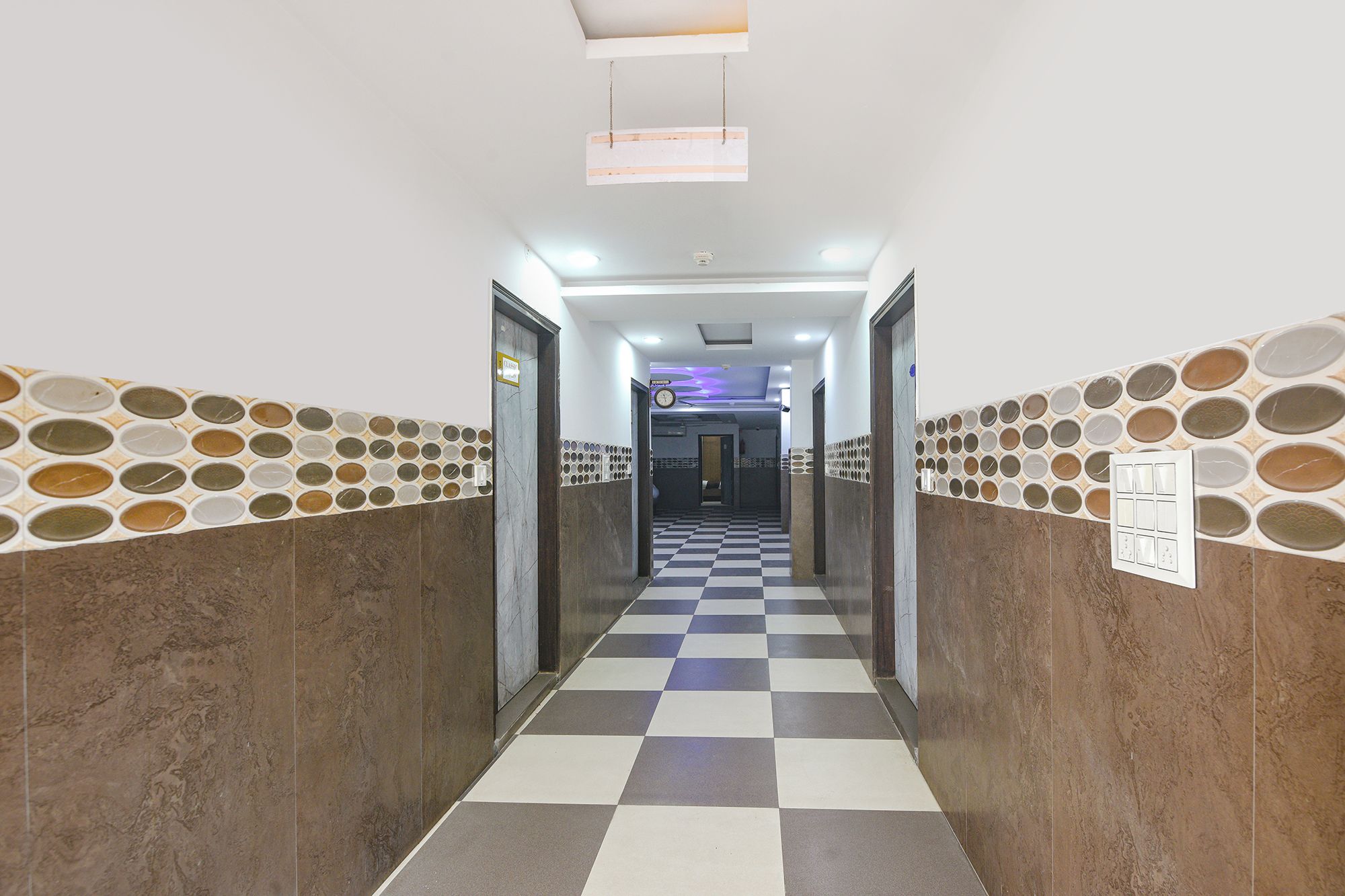 A hotel corridor with checkered flooring, patterned walls, and doors leading to rooms.