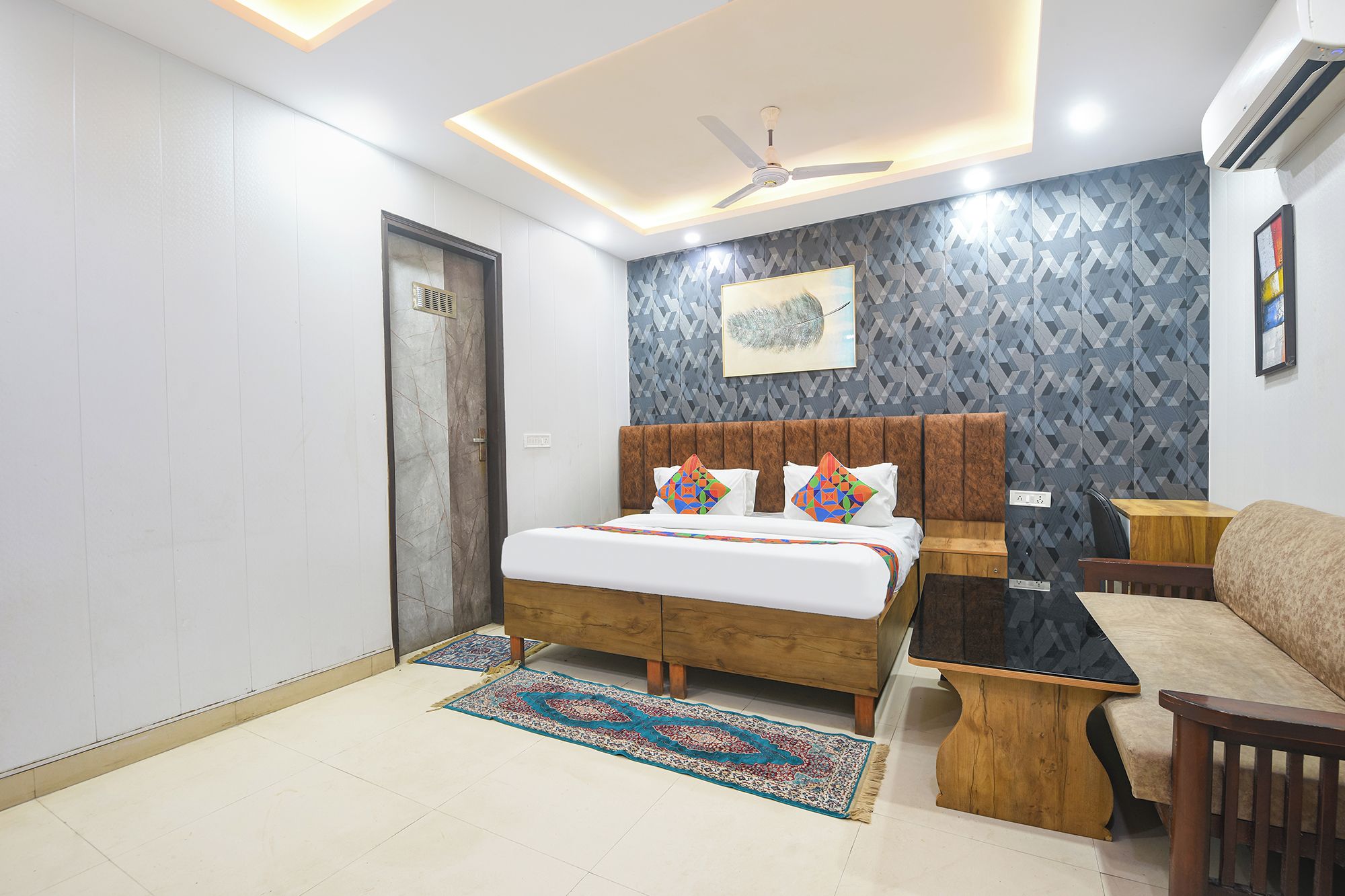 A bedroom with a bed, a wooden nightstand, a sofa, a ceiling fan, and a wall-mounted air conditioner.