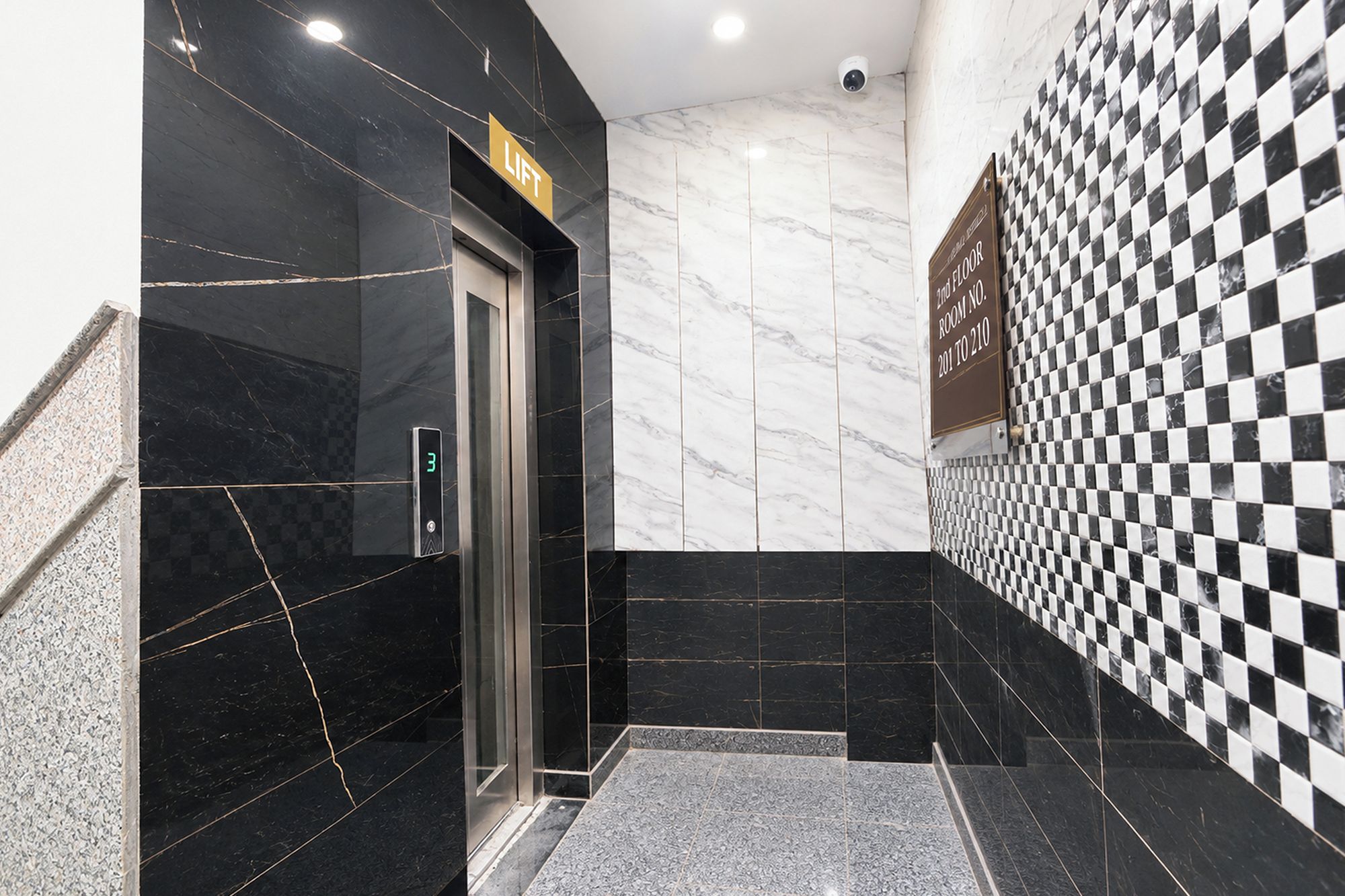 A modern elevator with a digital display, a checkered wall pattern, and a marble floor.