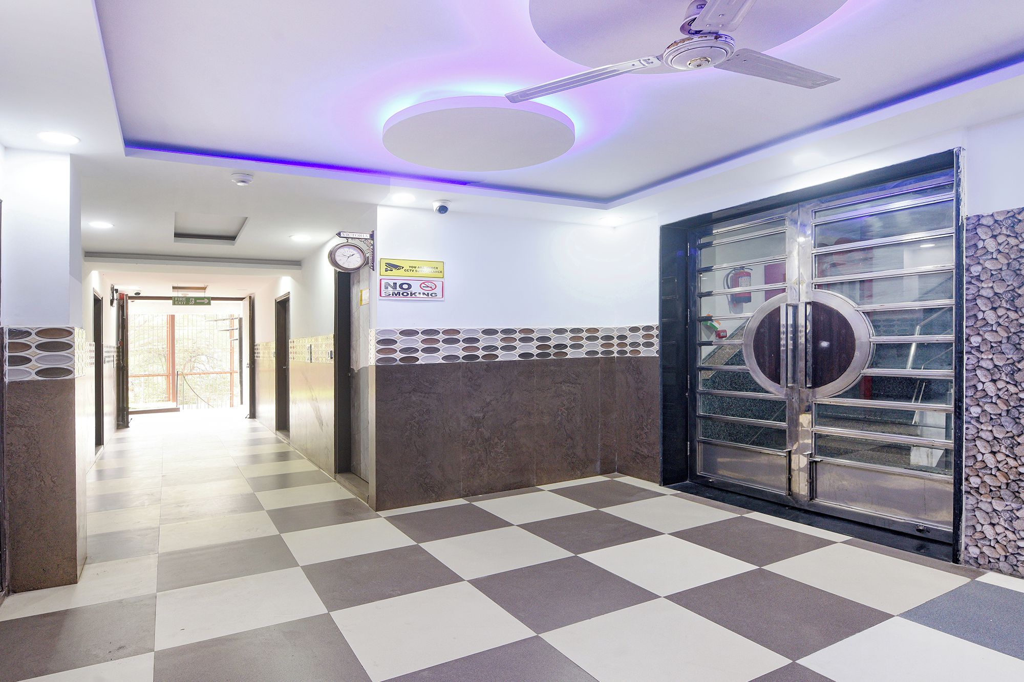 A hotel corridor with a checkered floor, a ceiling fan, and a door with a circular glass panel.