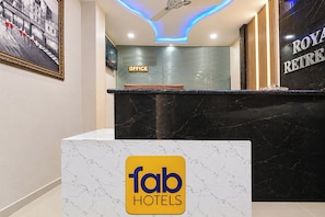 Uma área de recepção de hotel com balcão de mármore, placa indicando o escritório e o logotipo 'fab hotels'.