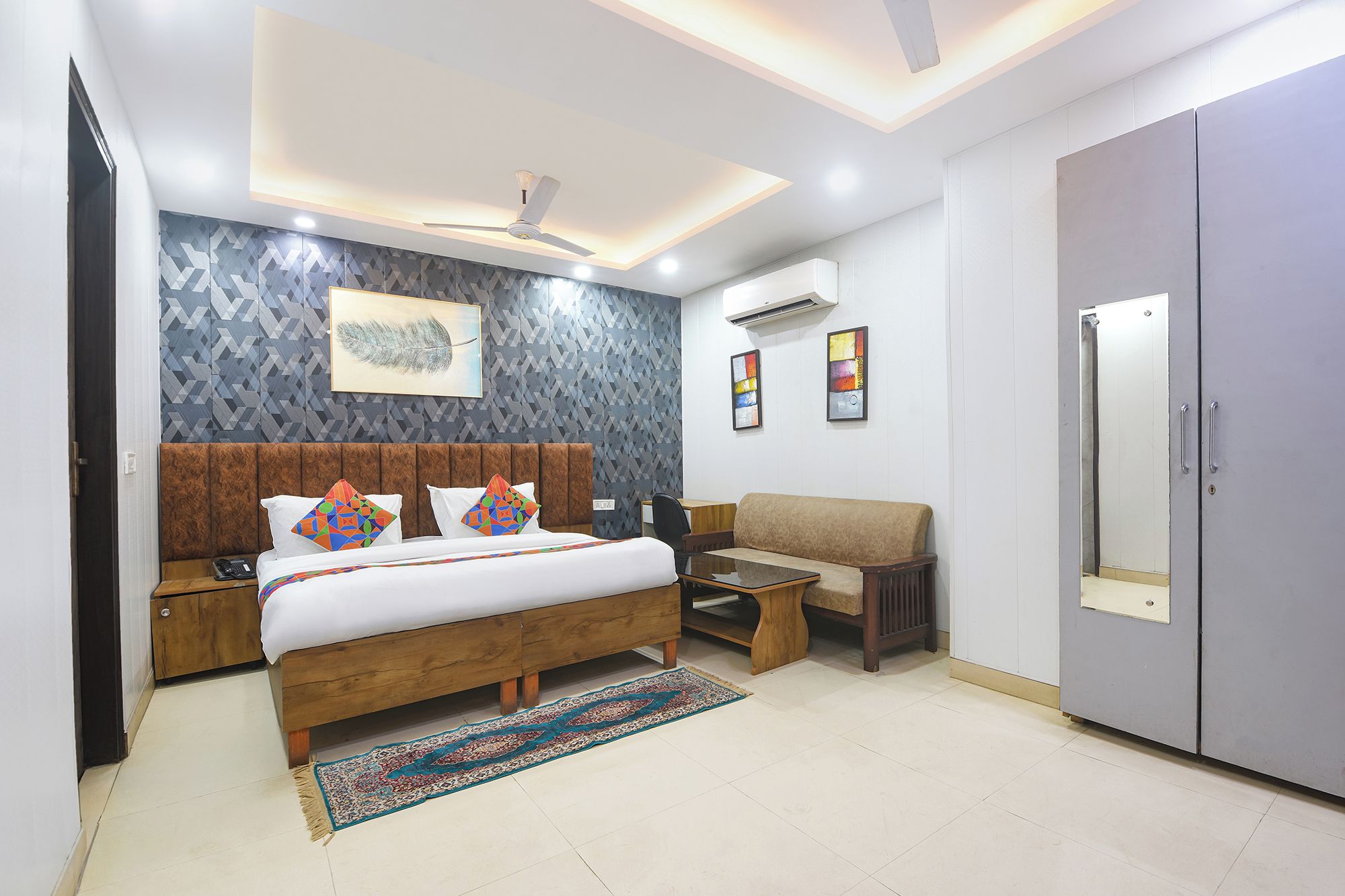 A bedroom with a bed, bedside tables, a sofa, a desk, a wardrobe, and a ceiling fan.