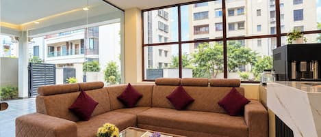 A modern living room with a sectional sofa, a glass coffee table, and a view of a residential building through large windows.